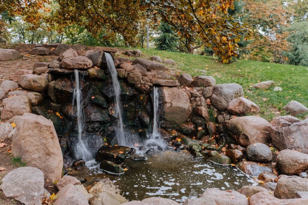 Peaceful waterfall surrounded by colorful autumn foliage and rocks in a park.