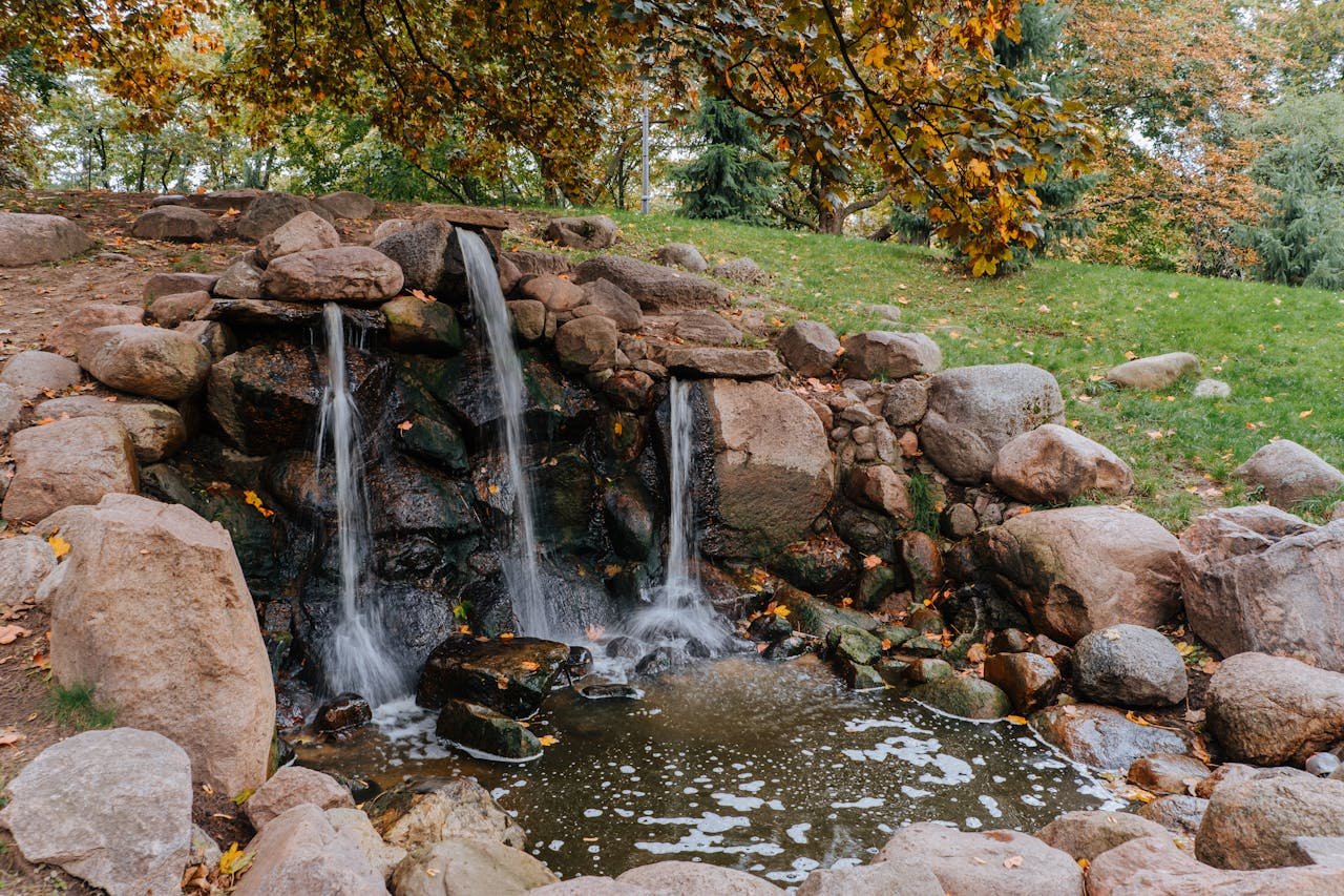 Peaceful waterfall surrounded by colorful autumn foliage and rocks in a park.